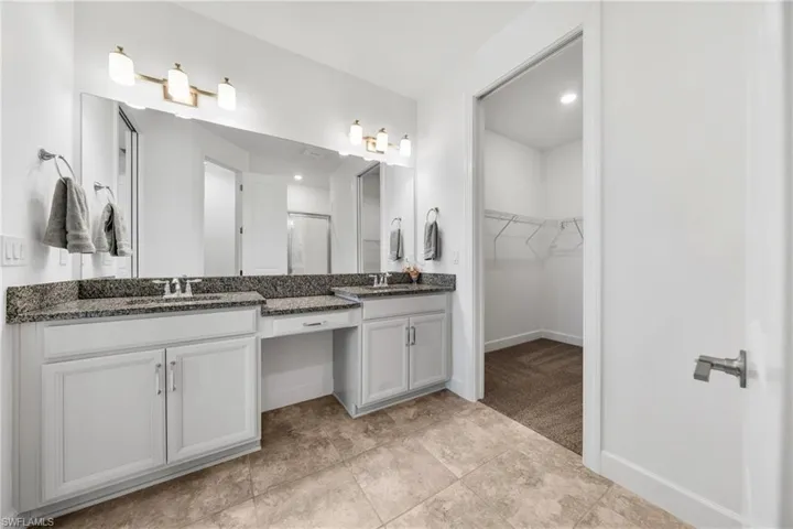 Double vanity featuring granite countertops with undermount sinks and brushed nickel faucets, white cabinetry, and a full-width mirror