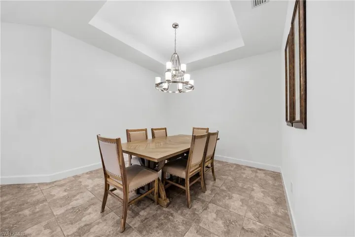 Dining area featuring a tray ceiling with a contemporary chandelier, neutral wall paint, and large format tile flooring
