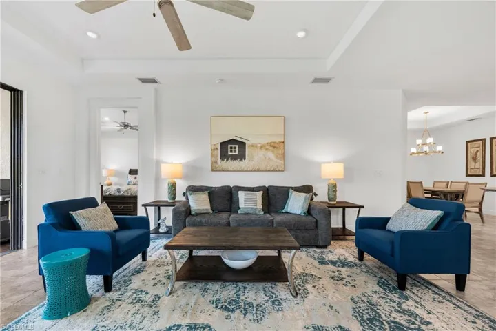 Open-concept living area featuring large format tile flooring, a tray ceiling with a ceiling fan, recessed lighting, and a kitchen with a breakfast bar