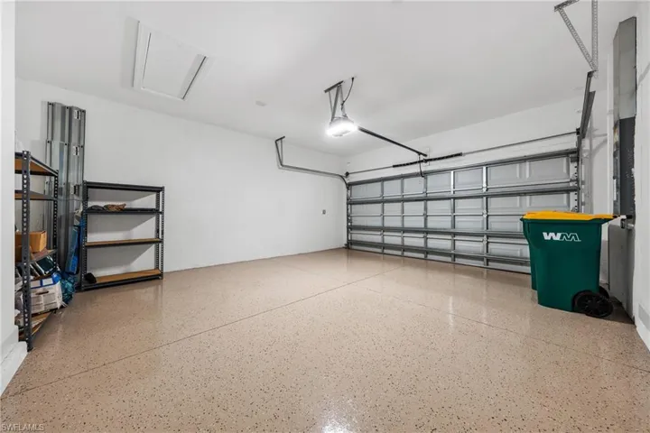 Spacious garage featuring a durable speckled epoxy floor, overhead lighting, an automatic garage door, and a ceiling-mounted access panel