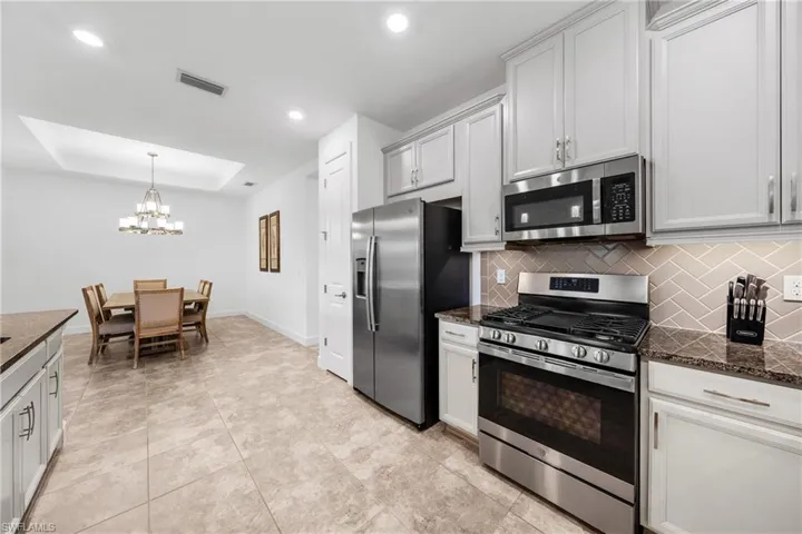Modern kitchen featuring stainless steel appliances, light cabinetry, granite-style countertops, and a herringbone tile backsplash