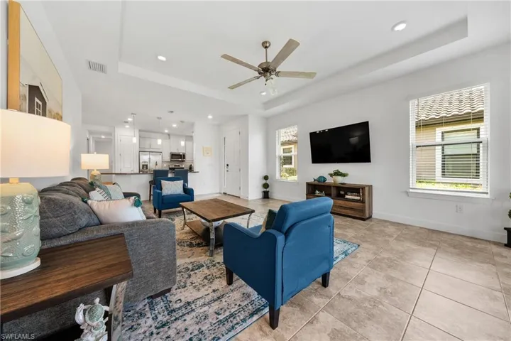 Open-concept living area featuring tray ceilings, recessed lighting, and tile flooring