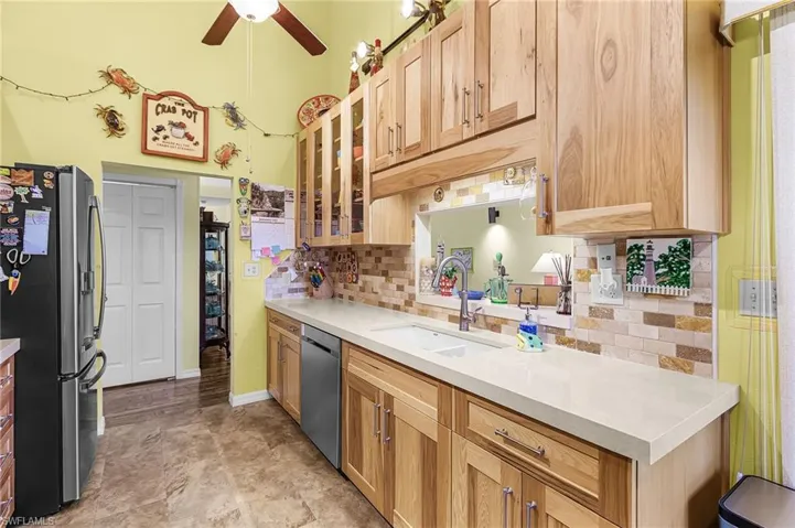 Kitchen featuring glass insert cabinets, appliances with stainless steel finishes, tasteful backsplash, a ceiling fan, and light brown cabinets