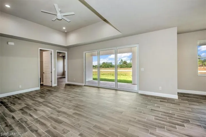 Unfurnished bedroom featuring a spacious closet, access to outside, wood tiled floors, a raised ceiling, and ceiling fan