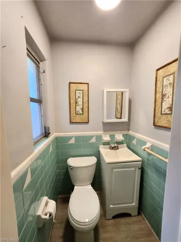 Bathroom with wood-type flooring, tile walls, and toilet