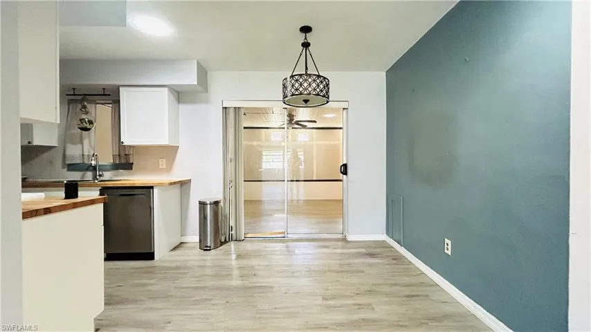 Kitchen featuring butcher block counters, hanging light fixtures, stainless steel dishwasher, white cabinets, and light wood-type flooring