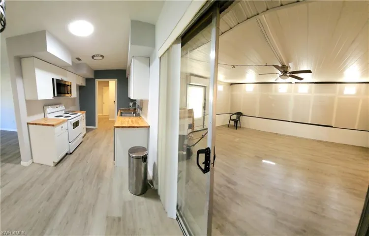 Enclosed porch with its own A/C  also Kitchen featuring butcher block counters, sink, white electric stove, ceiling fan, and white cabinetry