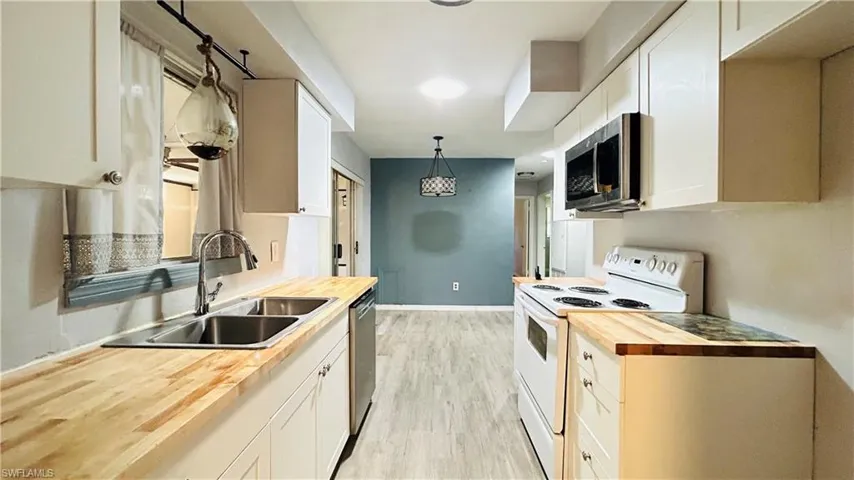 Kitchen with butcher block counters, pendant lighting, white cabinets, and stainless steel appliances