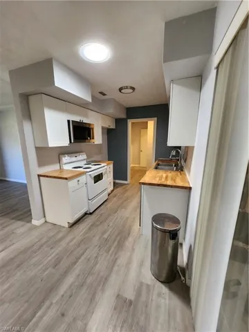 Kitchen with white cabinetry, sink, wood counters, stove, and light hardwood / wood-style floors