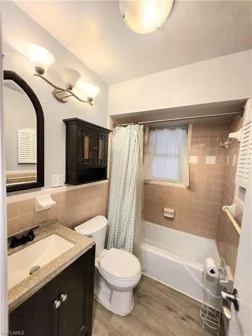 Full bathroom with vanity, shower / bath combo with shower curtain, hardwood / wood-style flooring, tile walls, and toilet