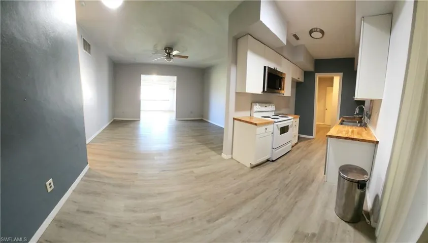 Kitchen with wood counters, white electric range, sink, ceiling fan, and white cabinetry