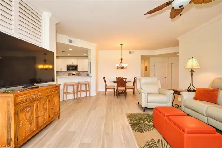 Living room featuring a ceiling fan, light wood-style floors, ornamental molding, and a chandelier