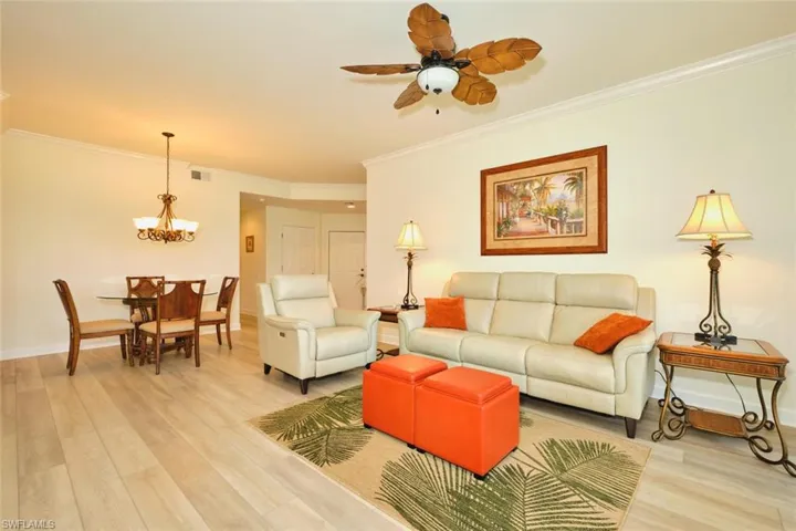 Living area featuring a chandelier, a ceiling fan, light wood-style flooring, crown molding, and baseboards