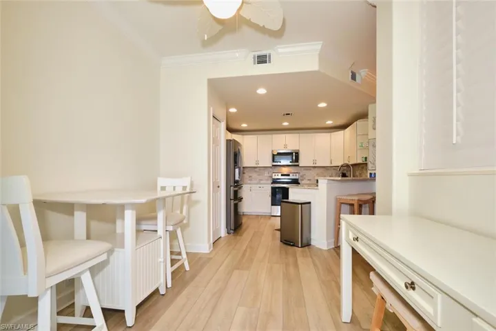 Kitchen with appliances with stainless steel finishes, ornamental molding, white cabinetry, tasteful backsplash, and light wood-style floors