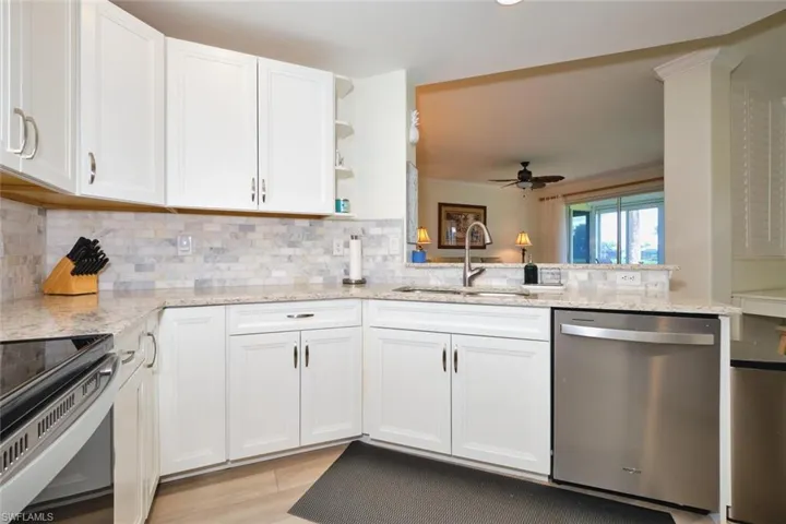 Kitchen with appliances with stainless steel finishes, a sink, a ceiling fan, white cabinets, and light stone counters