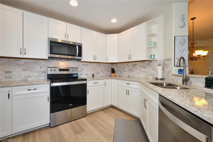 Kitchen with stainless steel appliances, a sink, white cabinets, open shelves, and tasteful backsplash