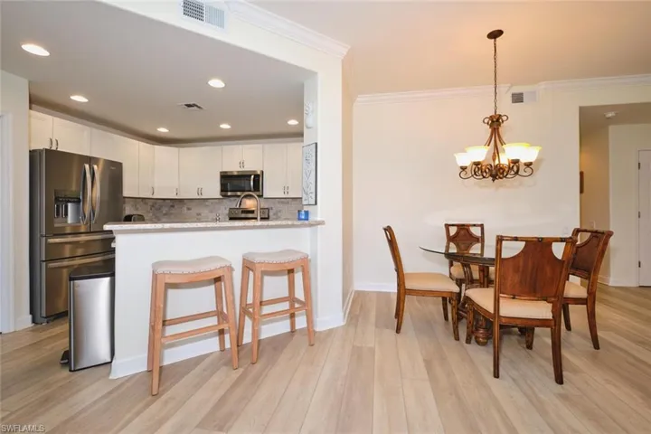 Kitchen featuring appliances with stainless steel finishes, crown molding, decorative backsplash, white cabinets, and light wood-style floors