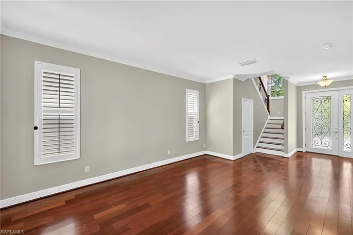 Empty room with ornamental molding, french doors, stairs, and dark wood-style flooring