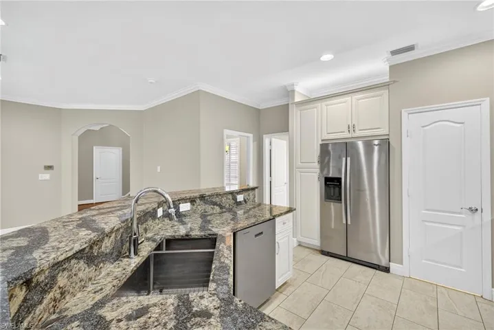 Kitchen with appliances with stainless steel finishes, dark stone countertops, crown molding, arched walkways, and recessed lighting