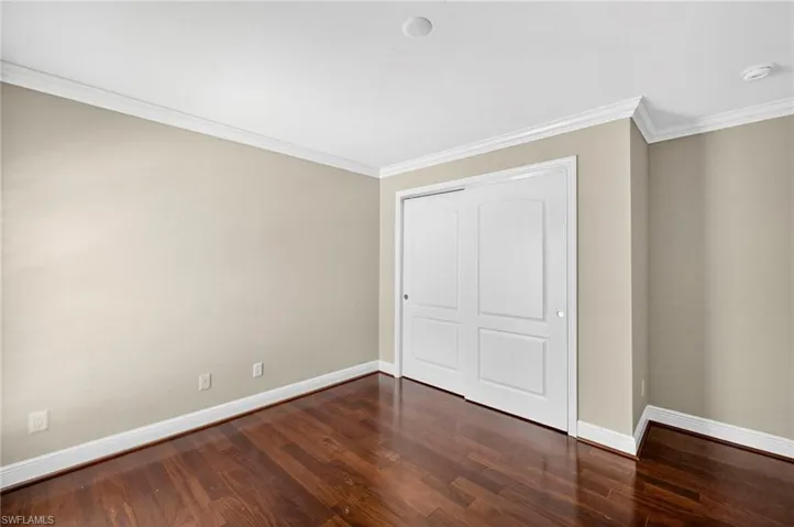 Unfurnished bedroom featuring crown molding, dark wood-style floors, and a closet
