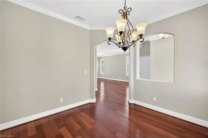 Unfurnished dining area with ornamental molding, arched walkways, dark wood-style floors, and a chandelier
