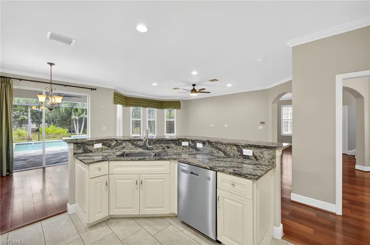 Kitchen featuring dark stone countertops, recessed lighting, stainless steel dishwasher, ornamental molding, and arched walkways