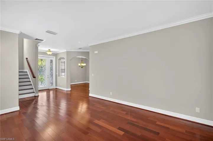 Empty room featuring arched walkways, stairway, crown molding, dark wood-style flooring, and a chandelier