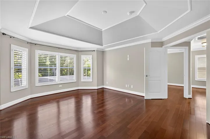 Empty room featuring a tray ceiling, dark wood-type flooring, and ornamental molding