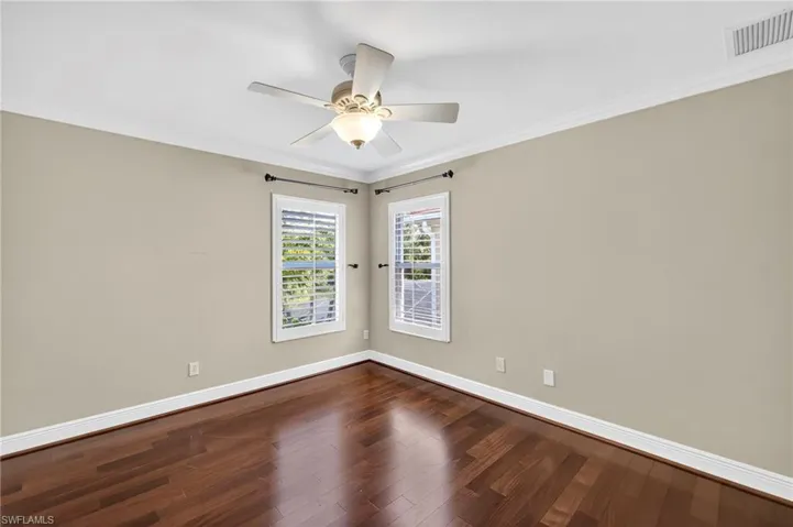 Empty room with crown molding, dark wood-style flooring, and ceiling fan