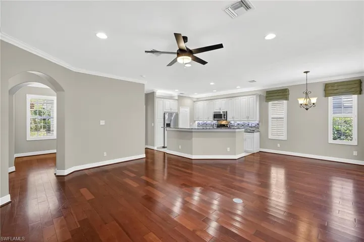 Unfurnished living room featuring crown molding, dark wood-style floors, arched walkways, recessed lighting, and a ceiling fan