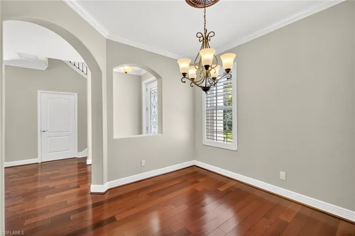 Unfurnished dining area with crown molding, arched walkways, a chandelier, and dark wood-style floors