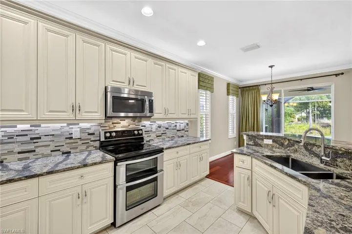 Kitchen featuring cream cabinets, stainless steel appliances, dark stone counters, ornamental molding, and recessed lighting