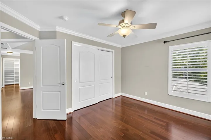 Unfurnished bedroom featuring crown molding, a closet, dark wood-style flooring, and ceiling fan