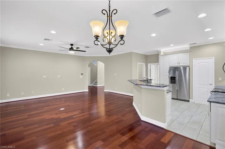 Kitchen featuring hanging light fixtures, arched walkways, stainless steel refrigerator with ice dispenser, crown molding, and a chandelier