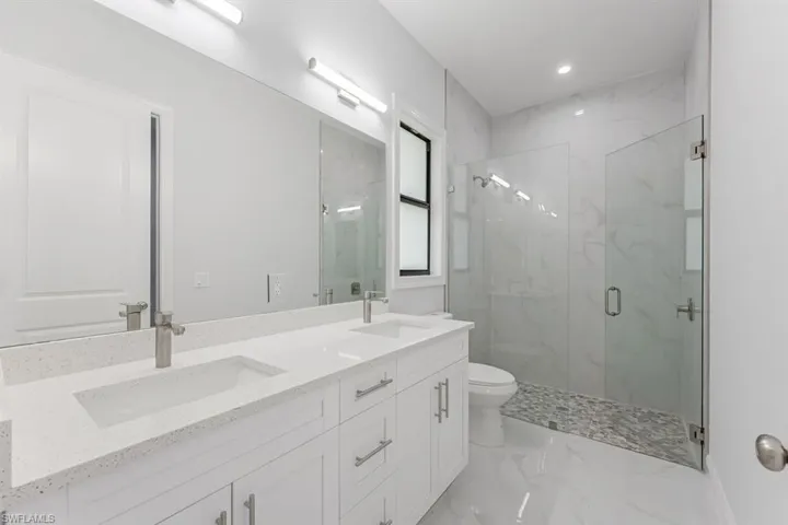 Bathroom with walk in shower, toilet, tile patterned floors, and double sink vanity