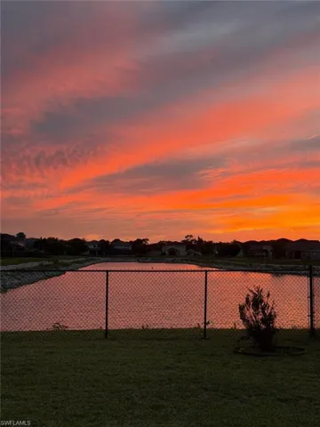 Expansive water feature bordered by a chain-link fence, featuring a manicured lawn foreground and distant residential structures