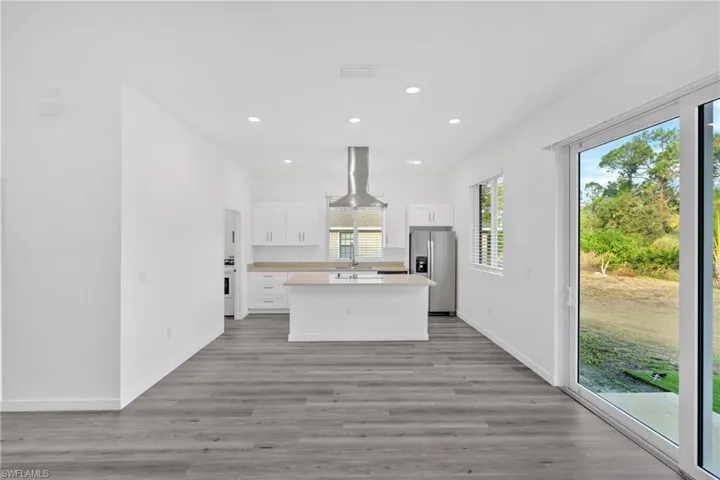 Kitchen with a center island, white cabinetry, light countertops, stainless steel fridge with ice dispenser, and island exhaust hood