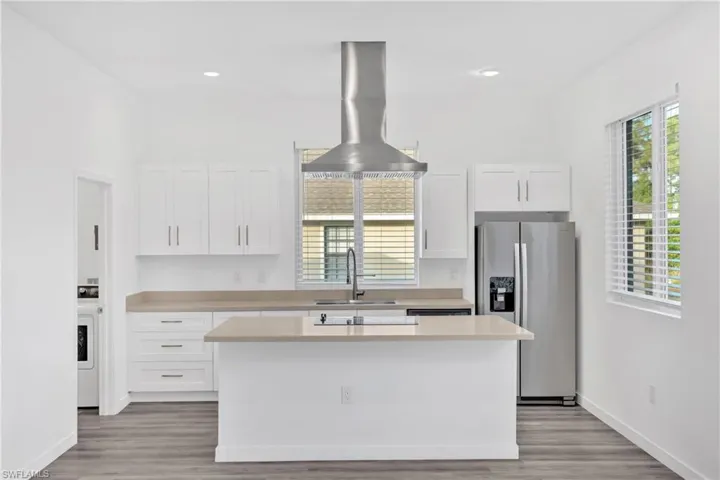 Kitchen featuring stainless steel fridge, white cabinets, healthy amount of natural light, island range hood, and recessed lighting