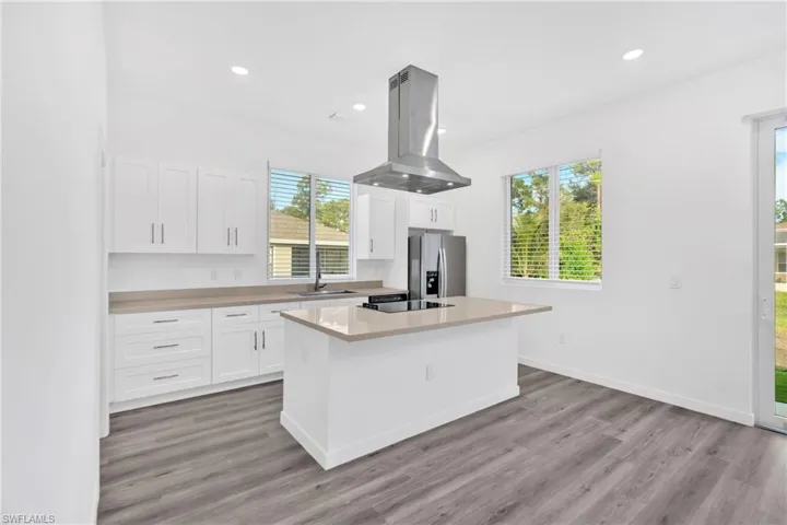 Kitchen with island exhaust hood, a kitchen island, white cabinetry, stainless steel fridge, and light wood-style flooring