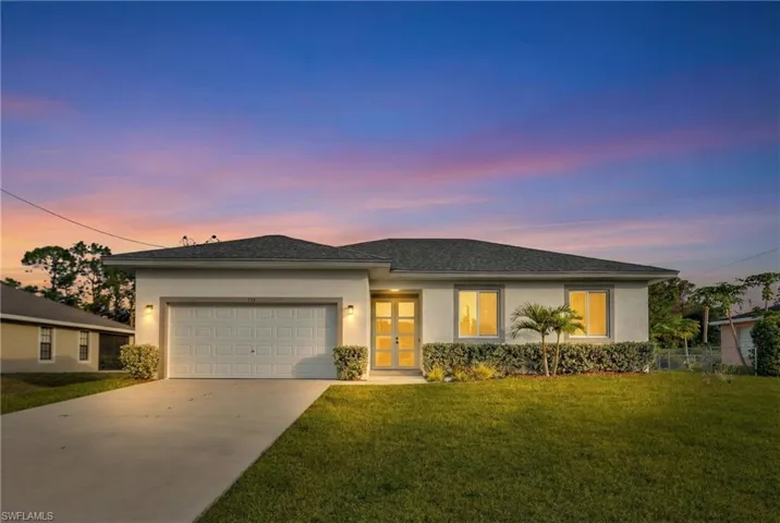 View of front of house featuring stucco siding, a lawn, concrete driveway, and an attached garage