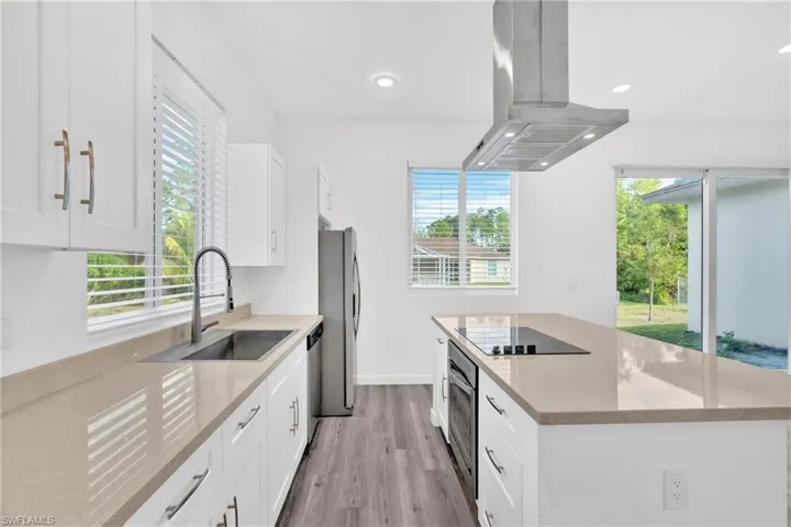 Kitchen featuring light stone countertops, a center island, white cabinetry, island range hood, and light wood-style flooring