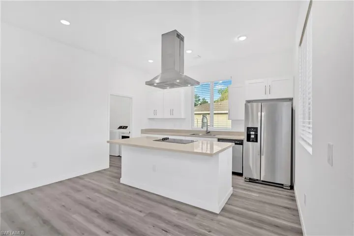 Kitchen with appliances with stainless steel finishes, a center island, white cabinets, island exhaust hood, and recessed lighting