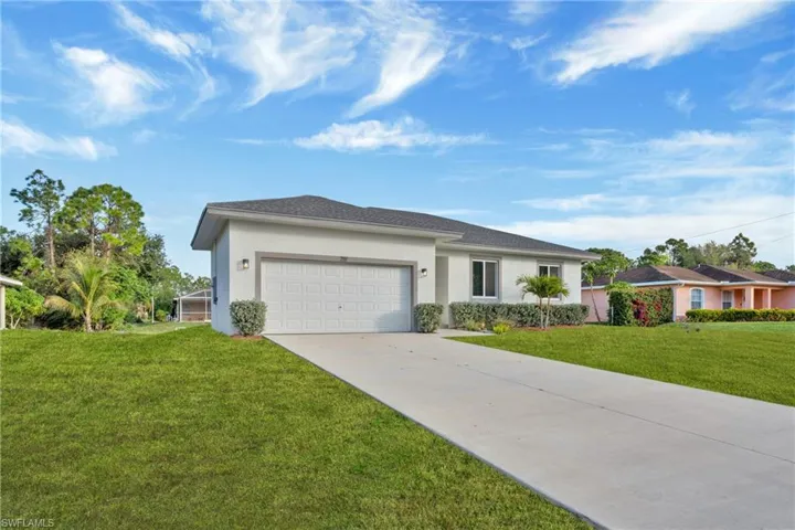 View of front of property featuring stucco siding, a front yard, an attached garage, and driveway