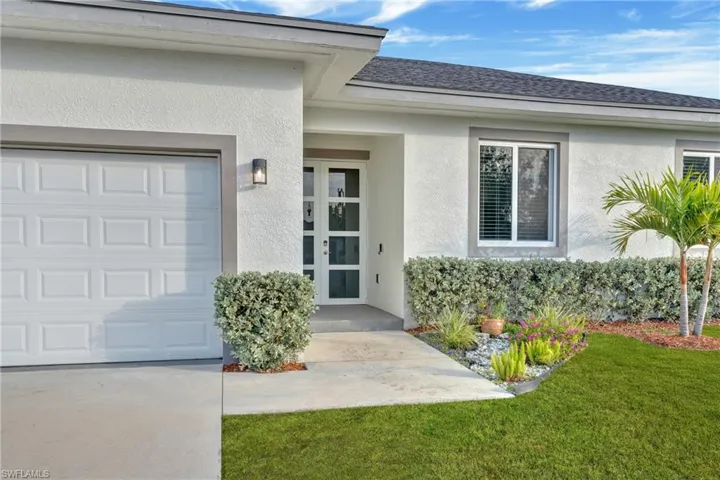 Entrance to property featuring stucco siding, roof with shingles, a garage, and a lawn
