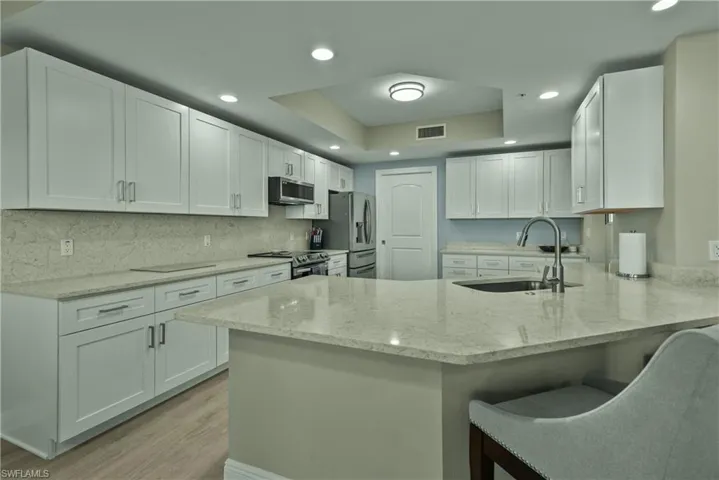 Kitchen with kitchen peninsula, sink, appliances with stainless steel finishes, light stone counters, and white cabinetry