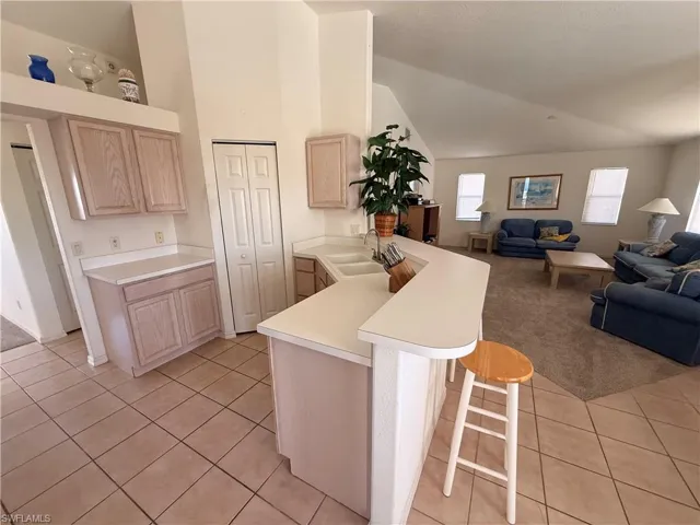Kitchen with light wood finish cabinets, a peninsula, light countertops, lofted ceiling, and a kitchen breakfast bar