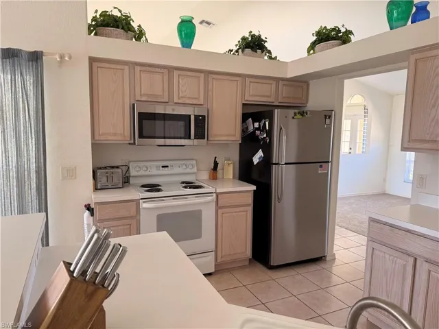 Kitchen with stainless steel appliances, light wood finish cabinets, light countertops, and light tile patterned floors