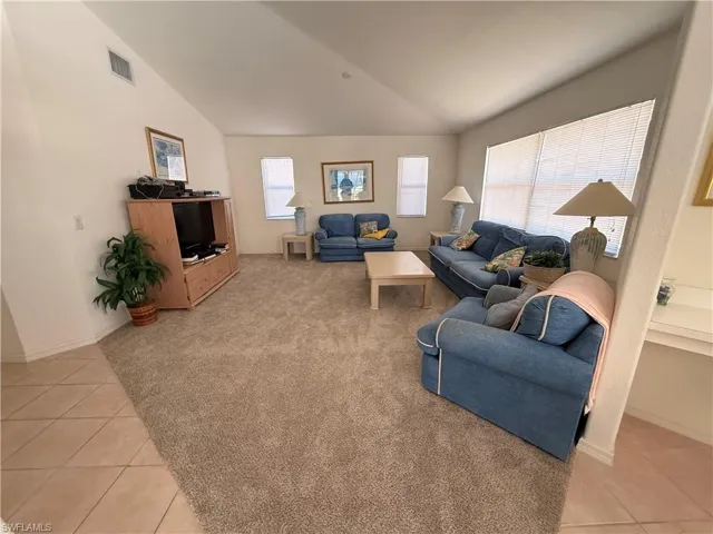 Living room with lofted ceiling, light tile patterned flooring, and light colored carpet