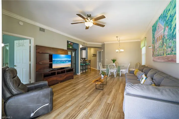 Living room featuring a ceiling fan, ornamental molding, light wood finished floors, and suspended lighting
