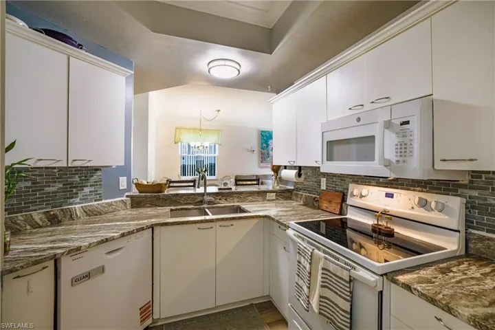 Kitchen with white appliances, white cabinetry, ornamental molding, decorative backsplash, and hanging lights